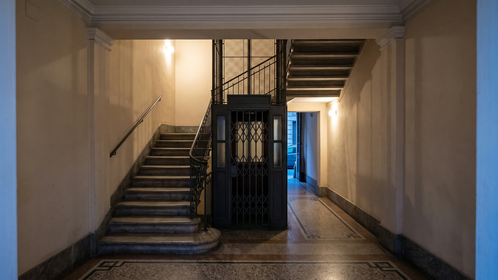 Androne di un palazzo milanese, con scala in pietra e ascensore storico.